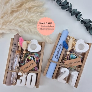 Könnte beinhalten: Zwei hölzerne Geschenkboxen mit Kerzen, Dekorationselementen und den Zahlen 30 und 21. Eine Box enthält eine braune Kerze mit Text, die andere eine blaue Kerze. Beide haben herzförmige Kerzenhalter.