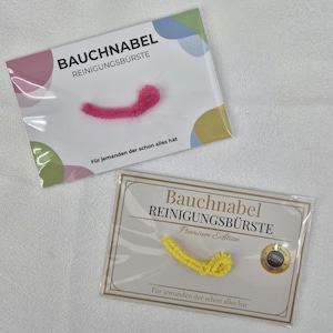 Könnte beinhalten: Zwei Packungen Bauchnabel-Reinigungsbürsten. Eine Packung hat eine rosa Bürste, die andere eine gelbe Bürste. Der Text auf den Packungen lautet "BAUCHNABEL REINIGUNGSBÜRSTE" und "Für jemanden der schon alles hat."