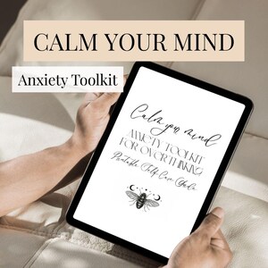 Puede incluir: Una tableta negra muestra el texto "Calm Your Mind" y "Anxiety Toolkit". La pantalla de la tableta muestra texto escrito a mano: "Anxiety Toolkit for Overthinking" y "Printable Self Care Guide". Un gráfico de abeja y media luna está en la parte inferior.