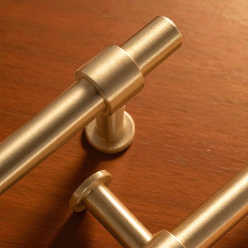 Close-up of brushed gold cabinet pull handle installed on a wooden surface.