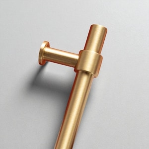 Pair of brushed gold cabinet pull handles placed on satin fabric background.
