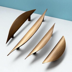 Könnte beinhalten: Vier bronzefarbene Schrankgriffe diagonal vor einem weißen und blauen Hintergrund angeordnet. Die Griffe haben ein geschwungenes, blattartiges Design mit einem kleinen, zylindrischen Sockel. Die Hardware besteht aus Metall und hat ein gebürstetes Finish.