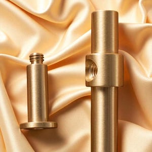 Brushed gold cabinet pull handle with detachable screw mounts displayed on satin fabric.