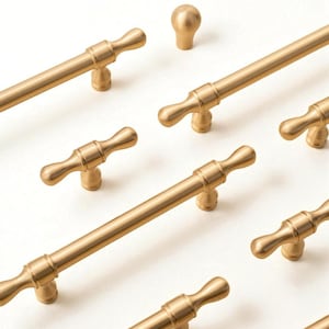 Może przedstawiać: Kolekcja złotych okuć do szafek, w tym uchwyty prętowe i gałka. Okucia mają klasyczny design z cylindrycznym prętem i dekoracyjnymi końcami. Gałka jest kulista. Ułożone na białym tle.