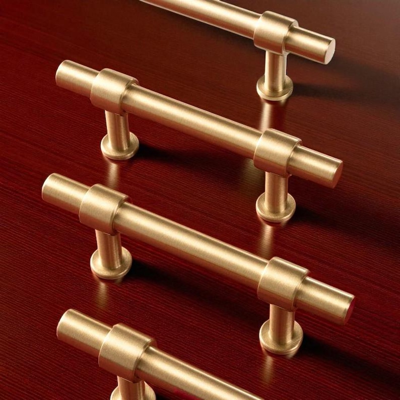 Multiple brushed gold cabinet pull handles installed on a wooden cabinet.