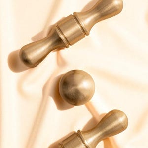 Close-up of brushed gold solid brass handles and knobs on satin fabric – minimalist luxury cabinet hardware.