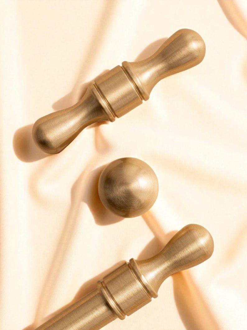 Close-up of brushed gold solid brass handles and knobs on satin fabric – minimalist luxury cabinet hardware.