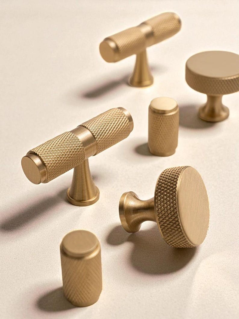 Modern gold brass handles and knobs displayed on neutral surface – minimalist cabinet hardware.