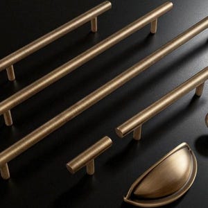 Peut inclure: Ensemble de quincaillerie de meubles de couleur bronze, comprenant plusieurs poignées de tirage de différentes longueurs, un bouton rond et une poignée cuvette. L'ensemble est présenté sur une surface sombre, mettant en valeur les différents styles et tailles.