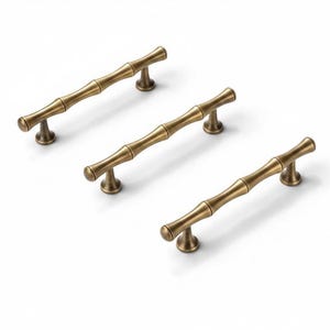 May include: Three antique brass cabinet pulls with a bamboo design. Each pull has a cylindrical handle with a series of rounded segments, mounted on a small, round base. The pulls are arranged diagonally against a white background.
