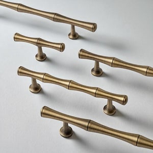 May include: Several bronze-colored cabinet pulls with a bamboo-inspired design are arranged on a white surface. The pulls have a cylindrical shape with a central, thicker section and rounded ends, and are mounted on a small, circular base.