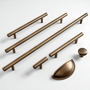以下が含まれることがあります： ブロンズ色のキャビネット金具のコレクション。長さの異なるバープル、小さなT字プル、丸いノブ、カッププルが含まれています。白い表面に配置され、さまざまなスタイルが示されています。
