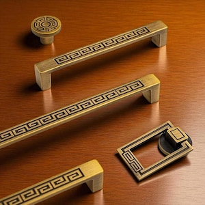 May include: A collection of antique brass cabinet hardware, including handles and a knob. The hardware features a black Greek key design. The handles are rectangular with a curved edge. The knob is round with a matching design.