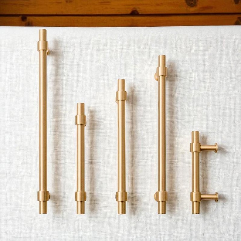 Set of modern brushed gold cabinet pull handles in multiple sizes displayed on white background.