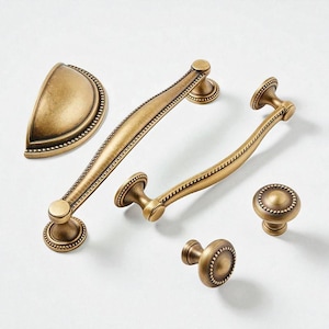 May include: An assortment of antique brass cabinet hardware, including two long handles, two knobs, and a cup pull. The hardware features a beaded edge design and a warm, aged finish, suitable for kitchen or furniture upgrades.