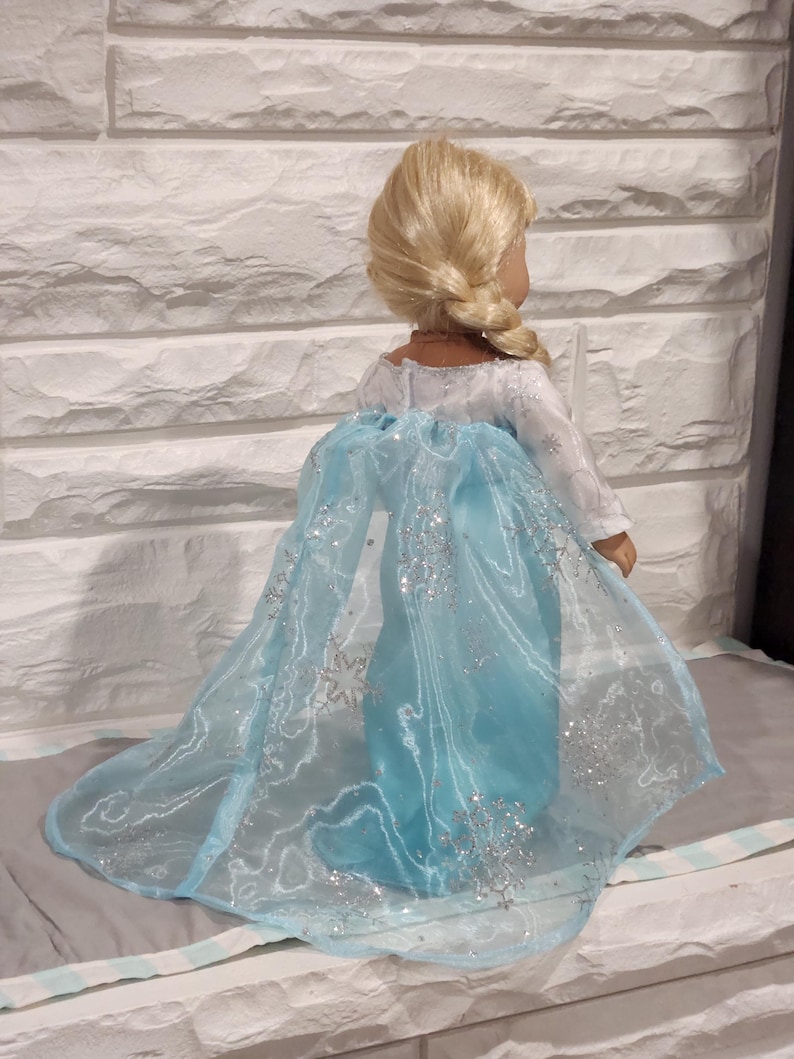 K&ouml;nnte beinhalten: Ein blaues und wei&szlig;es Puppenkleid mit einem glitzernden Umhang und Schneeflockenmuster. Das Kleid ist aus durchsichtigem Stoff und hat einen langen Schleier.