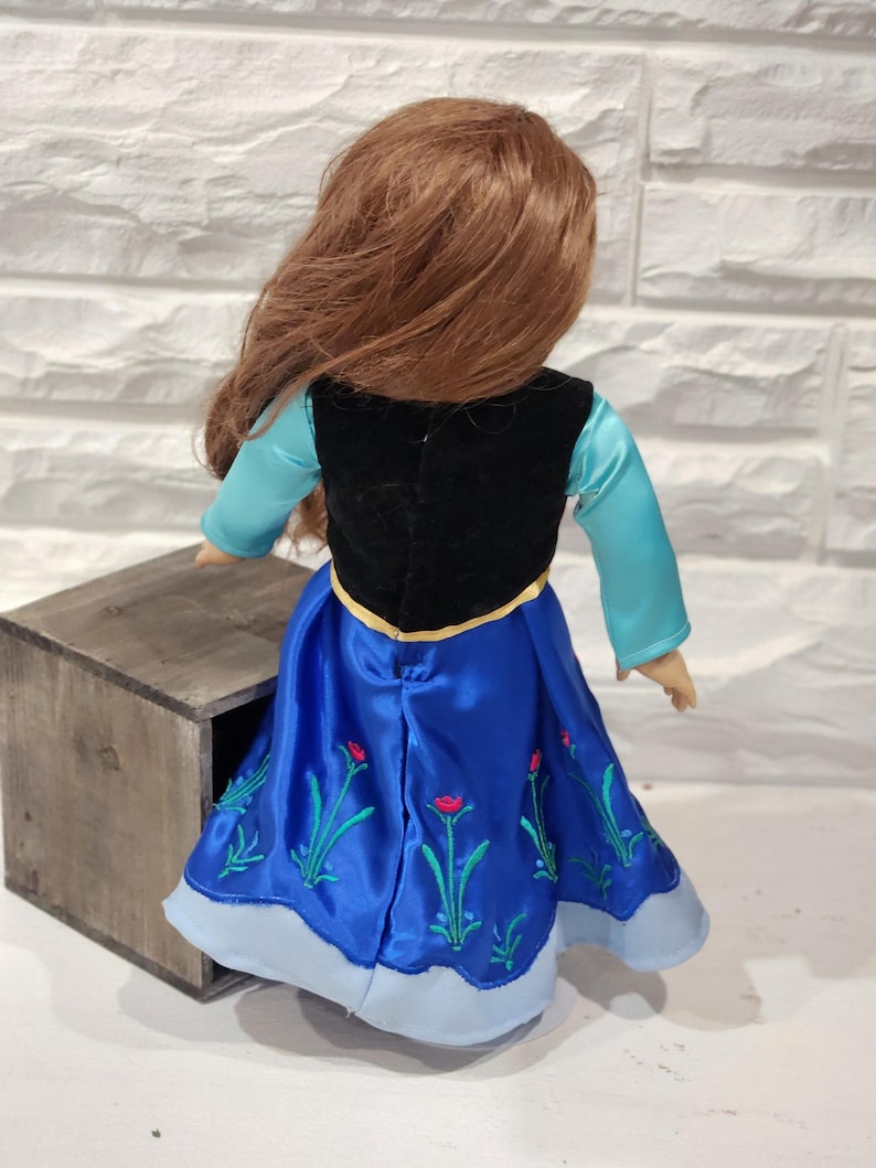 Pu&ograve; includere: Bambola con un vestito di raso blu con ricami floreali, un gilet nero e una maglia azzurra a maniche lunghe. La bambola ha lunghi capelli rossi. La bambola &egrave; accanto a una scatola di legno.