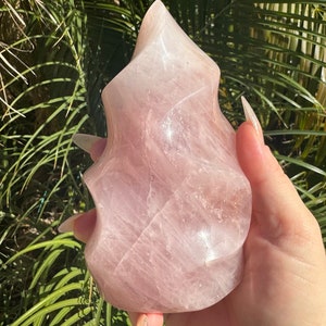 May include: A large, pink, rose quartz crystal carved into a unique, abstract shape. The crystal is smooth and polished, with a translucent appearance.