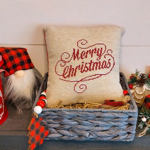 May include: A festive Christmas display featuring a red bucket with a bow, a gnome with a plaid hat, and a pillow embroidered with "Merry Christmas." A gray basket holds the pillow, and a sign that says "believe".