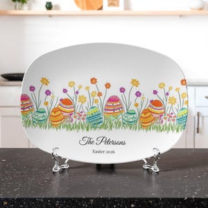 May include: White oval serving platter with a colorful Easter egg and floral design. The platter has a border of decorated eggs, flowers, and grass. The text "The Petersons" and "Easter 2026" are printed on the platter.