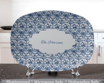 May include: A white oval serving platter with a blue and white floral pattern. The platter has a white oval label with the text "The Petersons" in blue cursive writing. The platter is on a silver stand.
