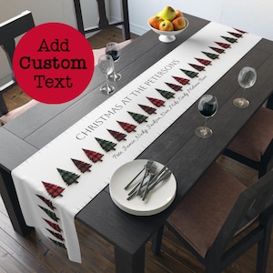May include: White table runner with a red and green plaid Christmas tree design. The text "CHRISTMAS AT THE PETERSONS" is printed on the runner, followed by a list of names.