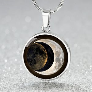 Puede incluir: Un collar de plata con un colgante redondo que presenta una imagen en blanco y negro de una luna creciente y una luna llena.