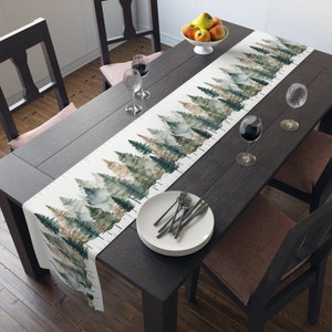 May include: A white table runner with a watercolour design of a forest. The runner is laid on a dark wood table with two chairs and a bowl of fruit.