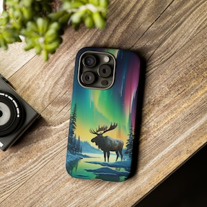 May include: A phone case with a colorful aurora borealis design and a silhouette of a moose standing in a snowy forest.