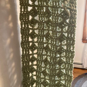 May include: A close-up of a crocheted green fabric with a repeating pattern of diamond shapes.