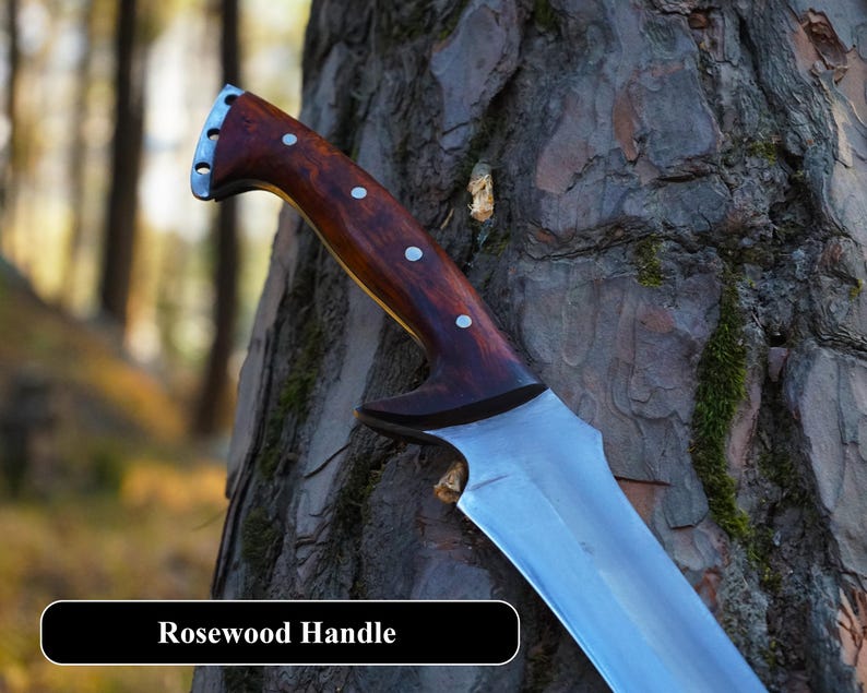 May include: A close-up of a knife with a rosewood handle and a silver blade. The knife is resting against a tree trunk. The text "Rosewood Handle" is visible at the bottom of the image.