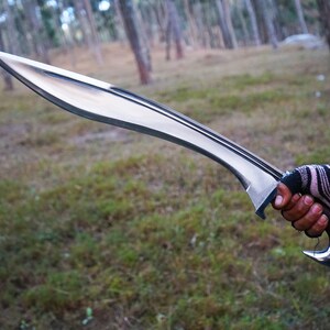 May include: A silver-colored sword with a curved blade and a wooden handle. The sword is held in a gloved hand.