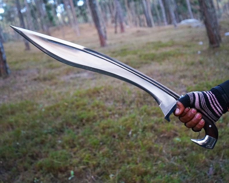 May include: A silver-colored sword with a curved blade and a wooden handle. The sword is held in a gloved hand.