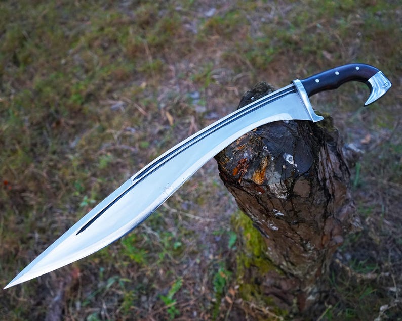 May include: A silver-colored sword with a black handle and a curved blade. The sword is resting on a tree stump.