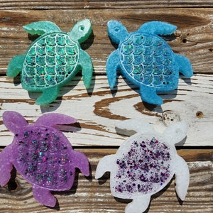 May include: Four resin turtle coasters with glitter embedded in the resin. The turtles are in shades of blue, green, purple, and white.