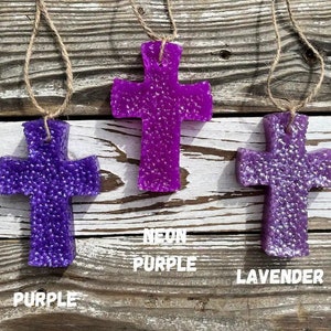 May include: Three purple cross-shaped air fresheners hanging from twine. The cross on the left is labeled "Purple", the middle cross is labeled "Neon Purple", and the cross on the right is labeled "Lavender".