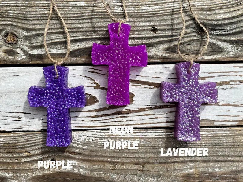 May include: Three purple cross-shaped air fresheners hanging from twine. The cross on the left is labeled "Purple", the middle cross is labeled "Neon Purple", and the cross on the right is labeled "Lavender".