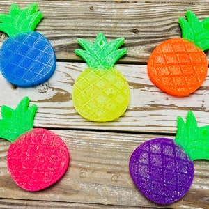 May include: Five pineapple-shaped ornaments with glitter. The pineapples are blue, yellow, orange, pink, and purple.