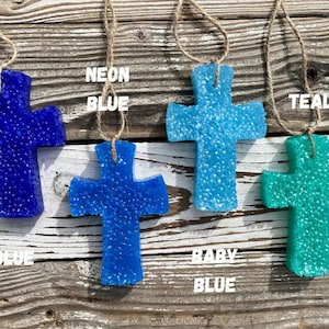 May include: Four car air fresheners shaped like crosses, hanging from twine. The crosses are blue, teal, and two shades of light blue. The text "NEON BLUE", "TEAL", "BABY BLUE" and "BLUE" are written below each cross.