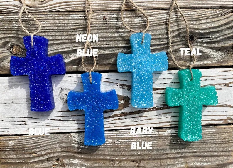 May include: Four car air fresheners shaped like crosses, hanging from twine. The crosses are blue, teal, and two shades of light blue. The text "NEON BLUE", "TEAL", "BABY BLUE" and "BLUE" are written below each cross.