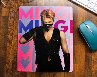 May include: Rectangular mousepad featuring a person with pink hair, wearing a black vest and gloves. The mousepad has a pink, blue, and white background with the name "MINGI" printed on it. A teal mouse and keyboard are visible.