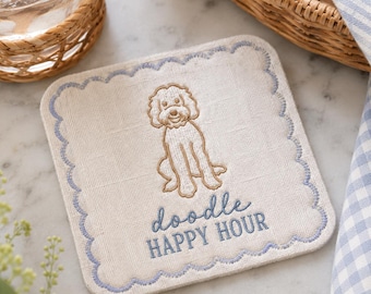 May include: A square beige fabric coaster with scalloped edges embroidered in light blue thread. The center features a tan embroidered doodle dog illustration above the blue embroidered text that reads doodle HAPPY HOUR.