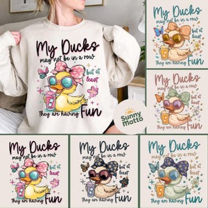 May include: Cream-colored sweatshirt with a graphic of a yellow duck wearing sunglasses and a bow, holding a drink. Text reads "My Ducks may not be in a row but at least they are having Fun."