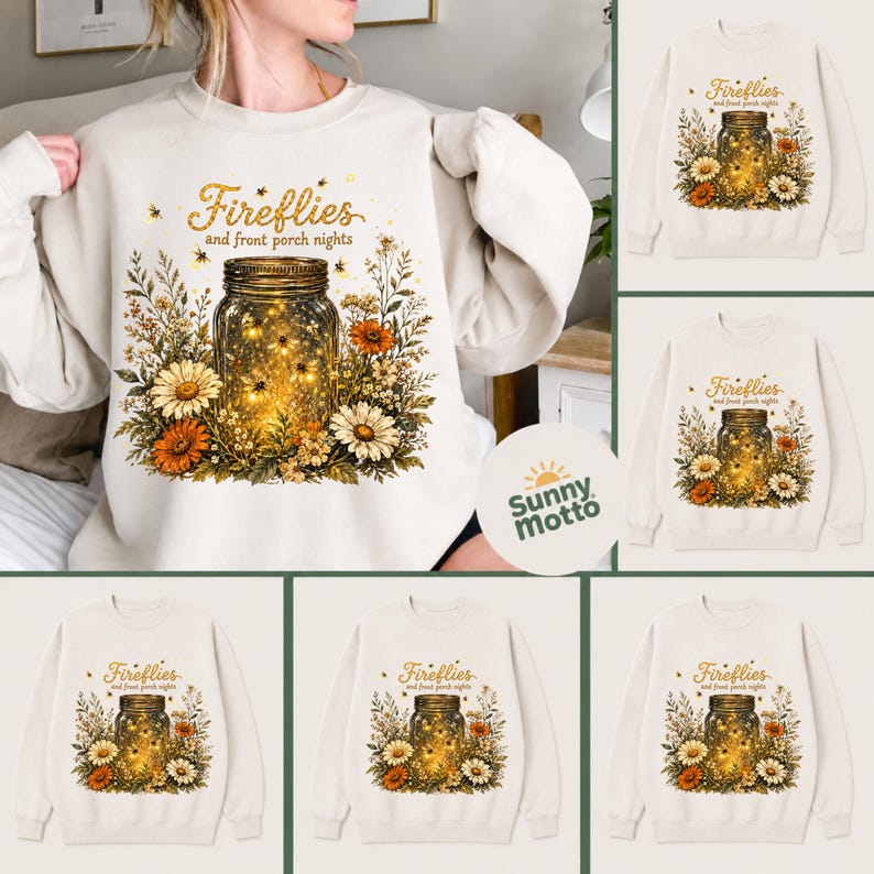May include: A cream-coloured sweatshirt with a graphic of a mason jar filled with glowing fireflies, surrounded by flowers. The text "Fireflies and front porch nights" is above the jar. The design includes orange and white daisies.