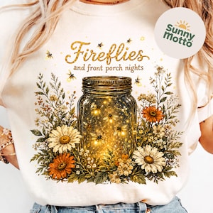 May include: White t-shirt with a design of a mason jar filled with fireflies, framed by flowers. The text "Fireflies and front porch nights" is above the jar in gold glitter. A Sunny Motto logo is on the right side of the shirt.