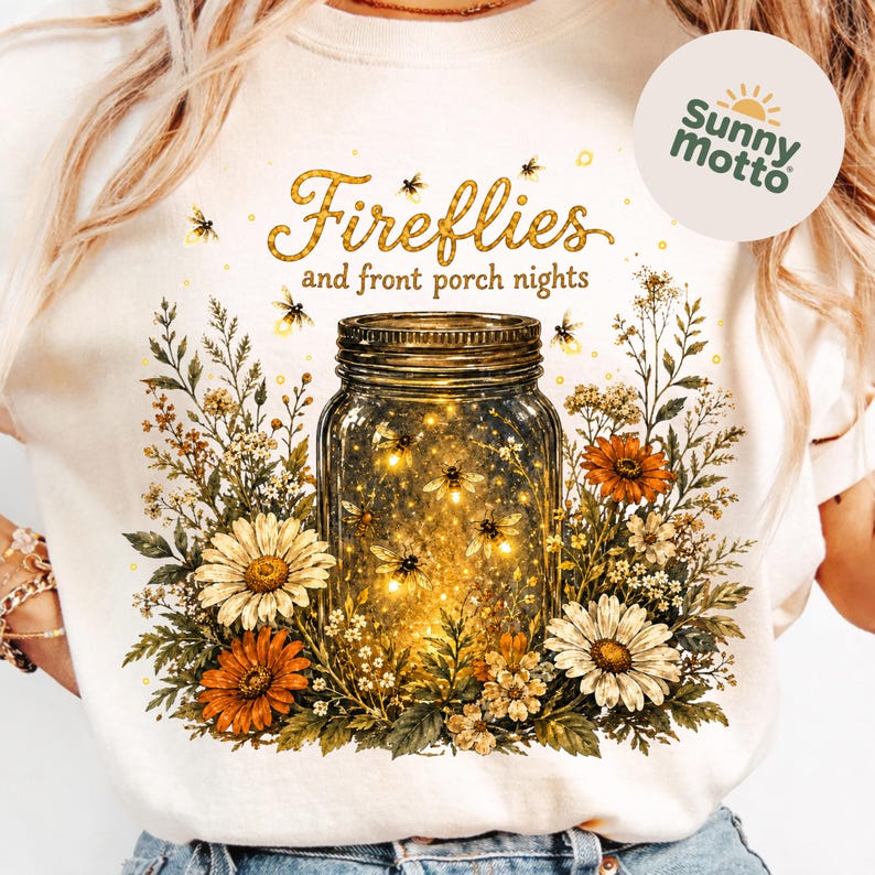 May include: White t-shirt with a design of a mason jar filled with fireflies, framed by flowers. The text "Fireflies and front porch nights" is above the jar in gold glitter. A Sunny Motto logo is on the right side of the shirt.