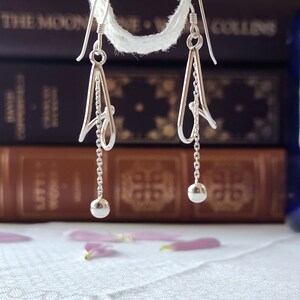 May include: Silver dangle earrings with a delicate, abstract design and a small ball at the end of each earring.