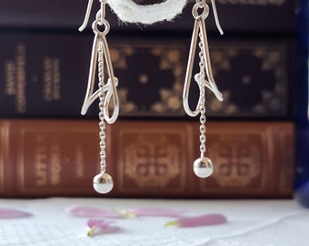 May include: Silver dangle earrings with a delicate, abstract design and a small ball at the end of each earring.