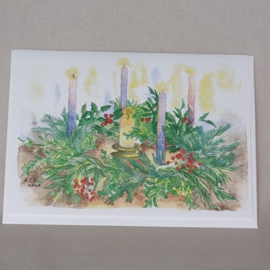 Card shows tabletop wreath of holly, boxwood, and pine with four lit candles around it and a thick central candle in a brass holder in the middle.  Candles cast light over the scene and entire picture glows.