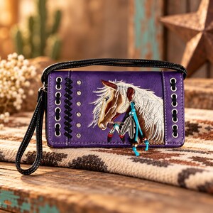 May include: A purple rectangular wristlet wallet featuring an embroidered horse head with a white mane. The wallet includes black lacing through silver metal grommets on both sides, a black wrist strap, and decorative dangling blue cord accents.